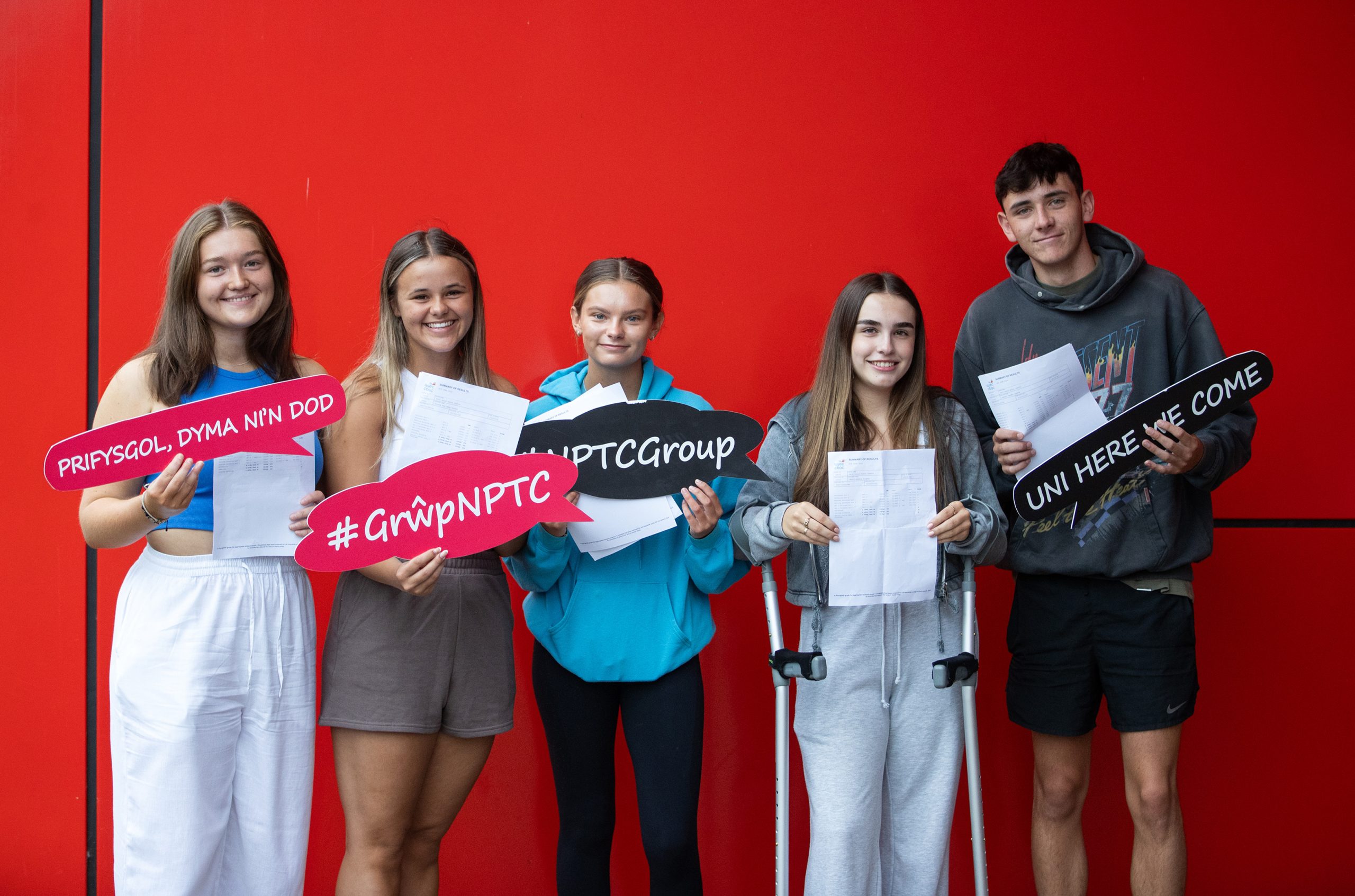 four female and one male student with their results slips and celebratory signs outside Neath College.